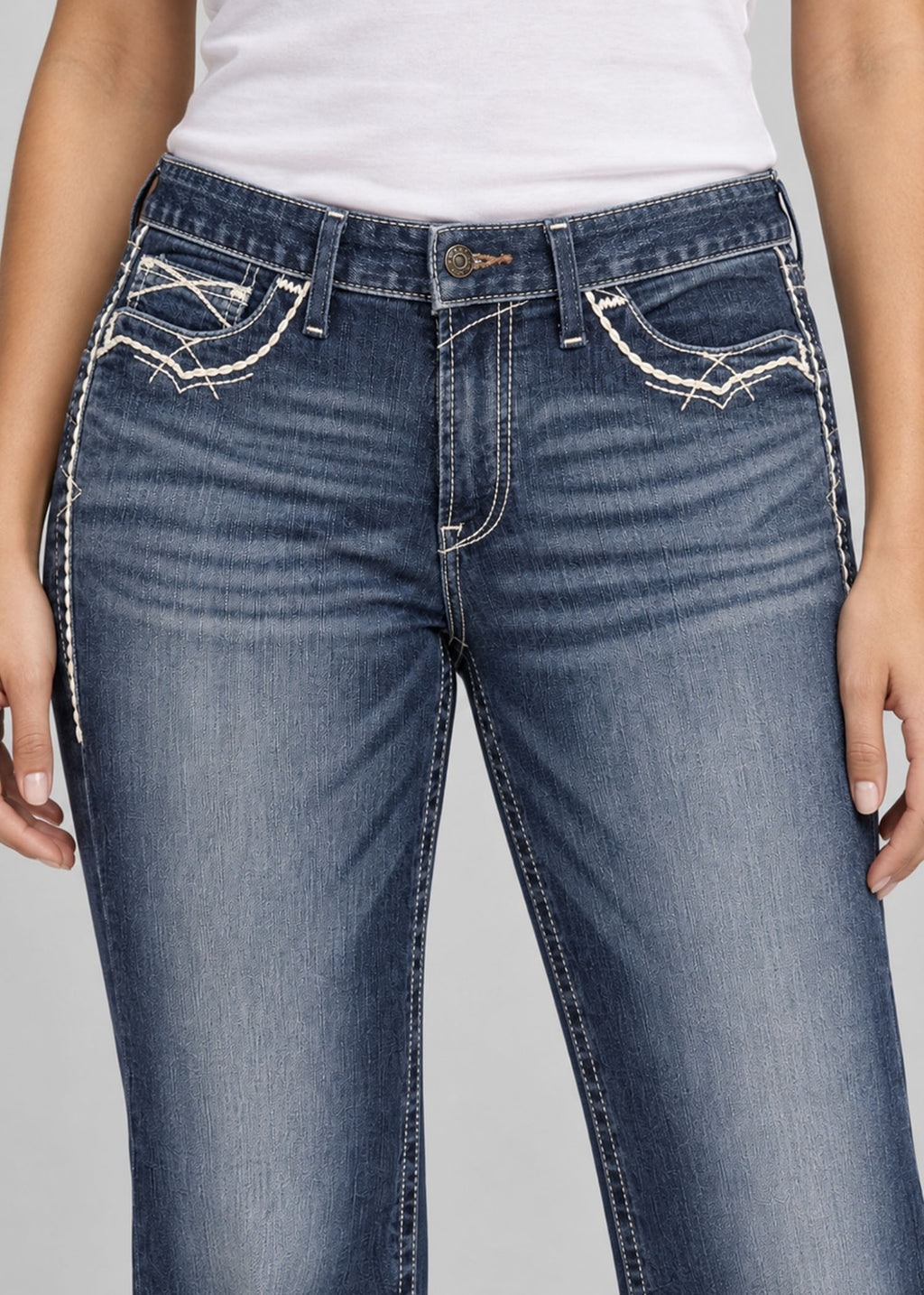 Blue wash bootcut jeans on female model, embroidered front pockets close up